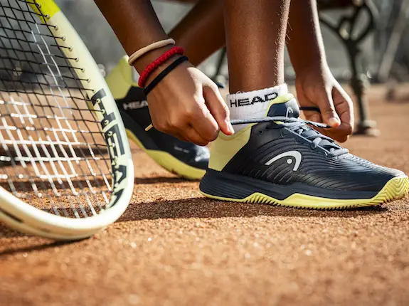 female tying up his tennis show with a head tennis racquet in the foreground