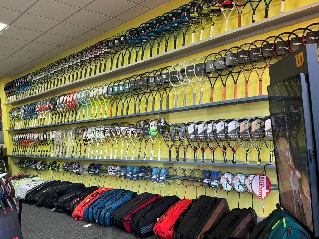 large range of tennis racquets for sale across 4 rows of shelves in a shop